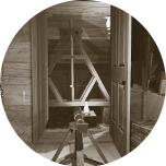 A small circular image containing an image of Kater's Pendulum as seen from the officer's quarters inside the expedition house. The pendulum hangs in an 'A' shaped wooden frame inside one of the lean to structures at each end of the house. Clicking this image will start the 'Katers Pendulum game' 