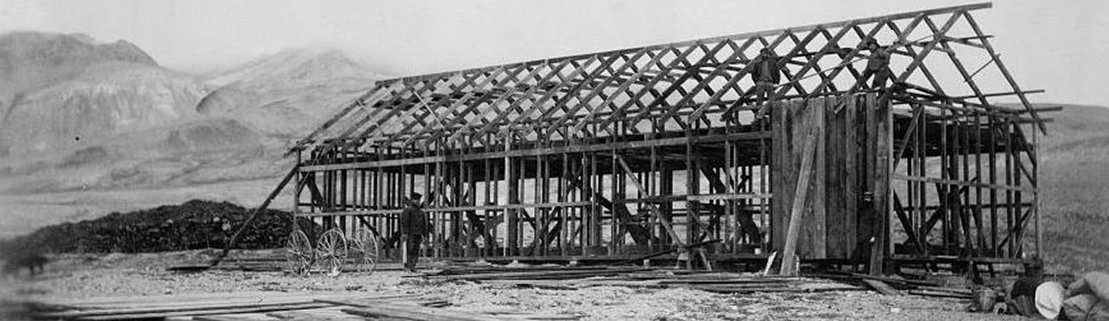 Historic photograph showing the completed house frame of the Lady Franklin Bay Expedition headquarters. In this photograph, the arched roof has been completed. Two figures stand on the roof frame adding wall boards.