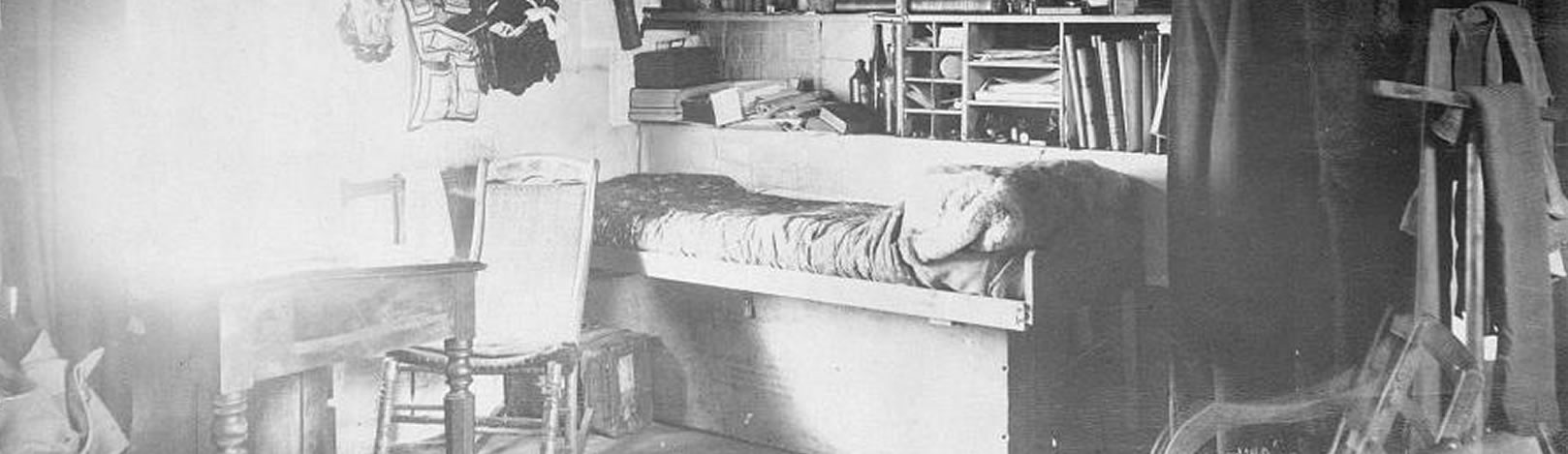 Historic photograph of Greely’s quarters, showing his bed, desk, and bookshelves. A window near the desk illuminates the room.
